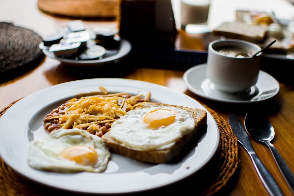 A breakfast spread consisting of two sunny-side-up eggs with home fries and a cup of coffee on a table.