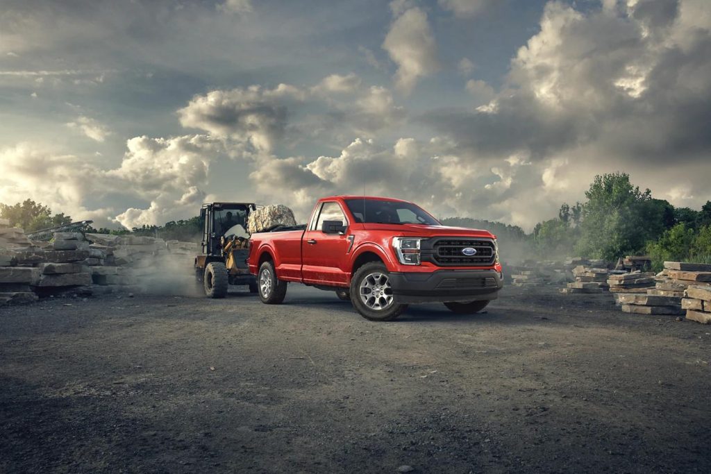 A red 2022 Ford F-150 parked on top of gravel at a construction site. Mountains and several clouds are visible in the background.