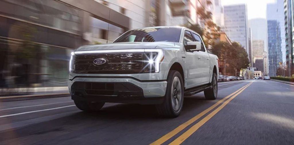 A white 2023 Ford F-150 Lightning driving down a city road.