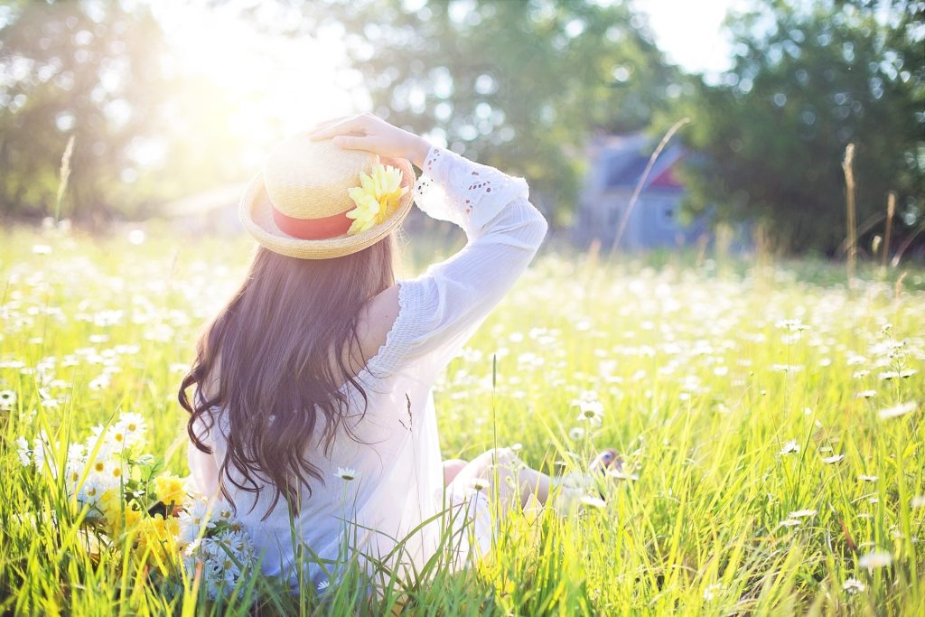 A woman facing away from the camera laying in a field of flowers and is wearing a sunhat.