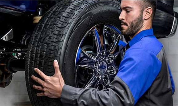 A Ford technician changing a vehicle tire with OEM parts.