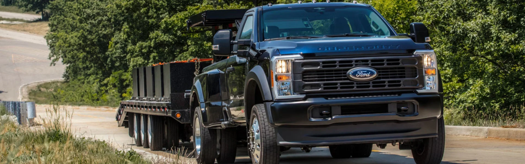A Ford Super Duty truck towing a large flatbed trailer on a road surrounded by trees.