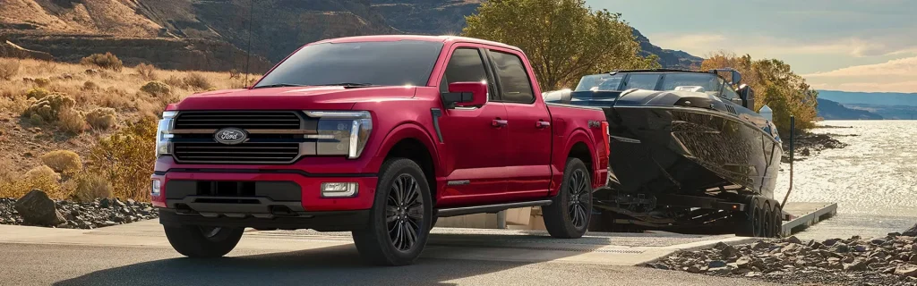 A red Ford F-150 truck towing a boat on a trailer along a scenic, rocky path near water.